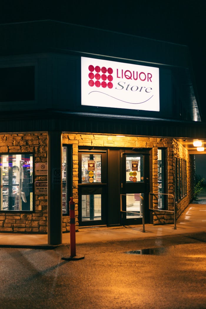 Nighttime view of a well-lit liquor store entrance with signage and brick facade.